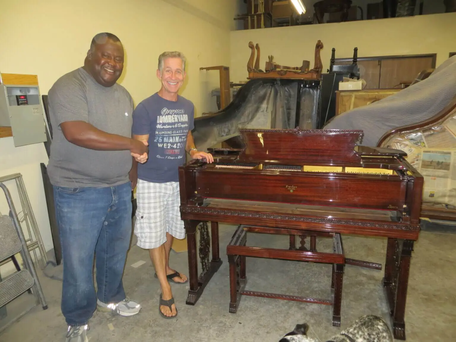Two men standing next to a piano in a room.