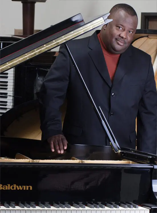 A man standing next to a piano in front of a keyboard.